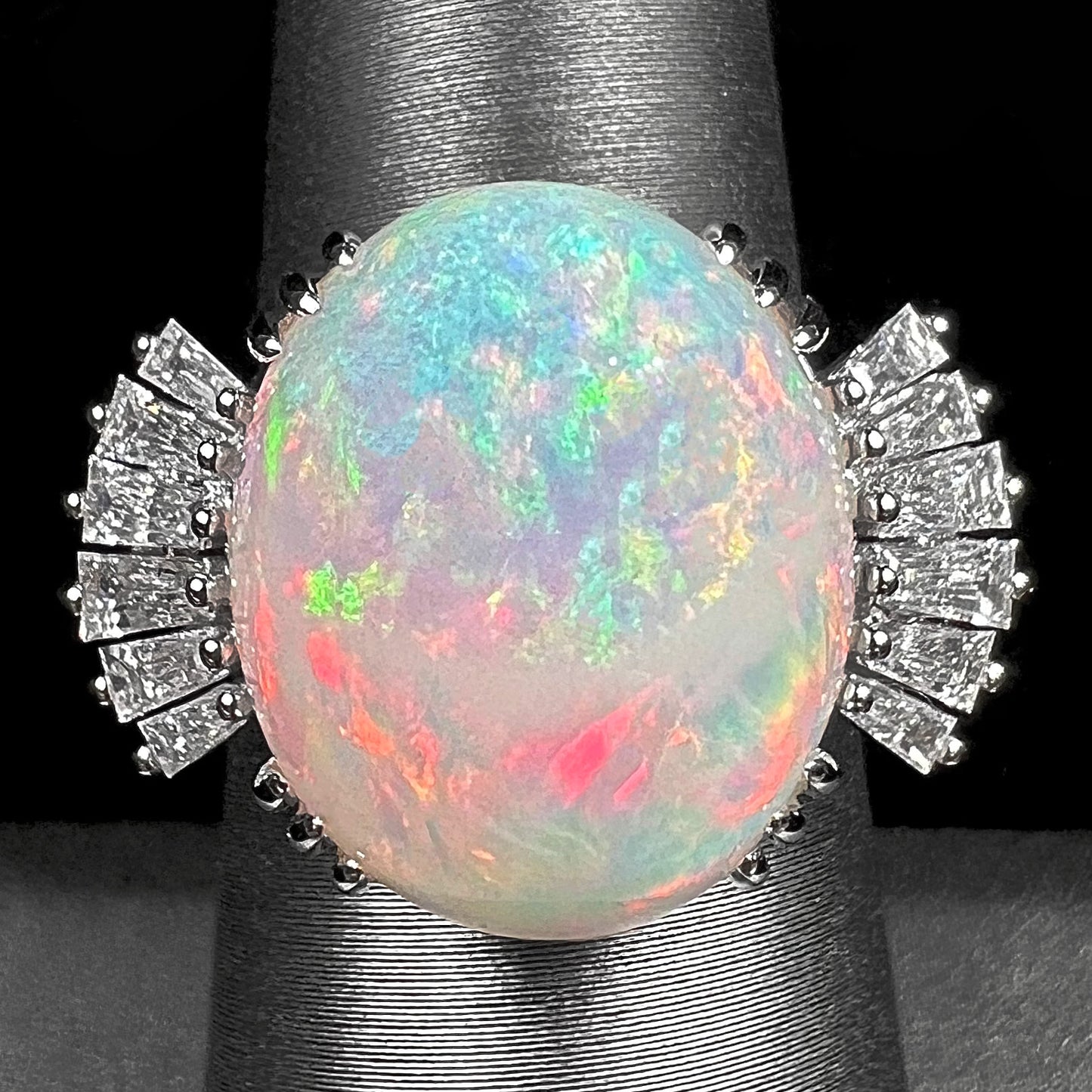 An oval cabochon cut opal mounted in a ladies' white gold ring between tapered baguette cut diamonds.