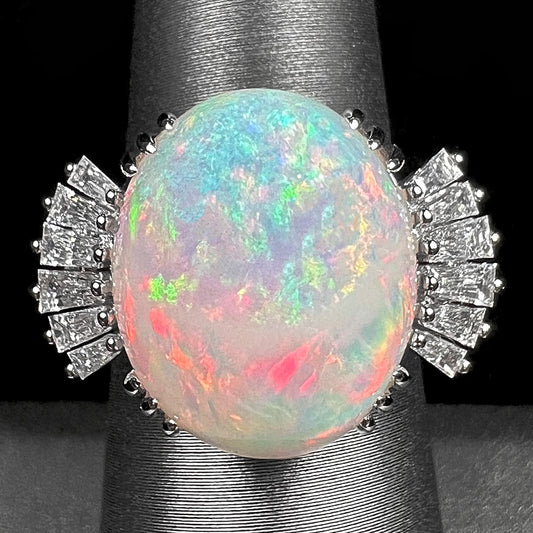 An oval cabochon cut opal mounted in a ladies' white gold ring between tapered baguette cut diamonds.