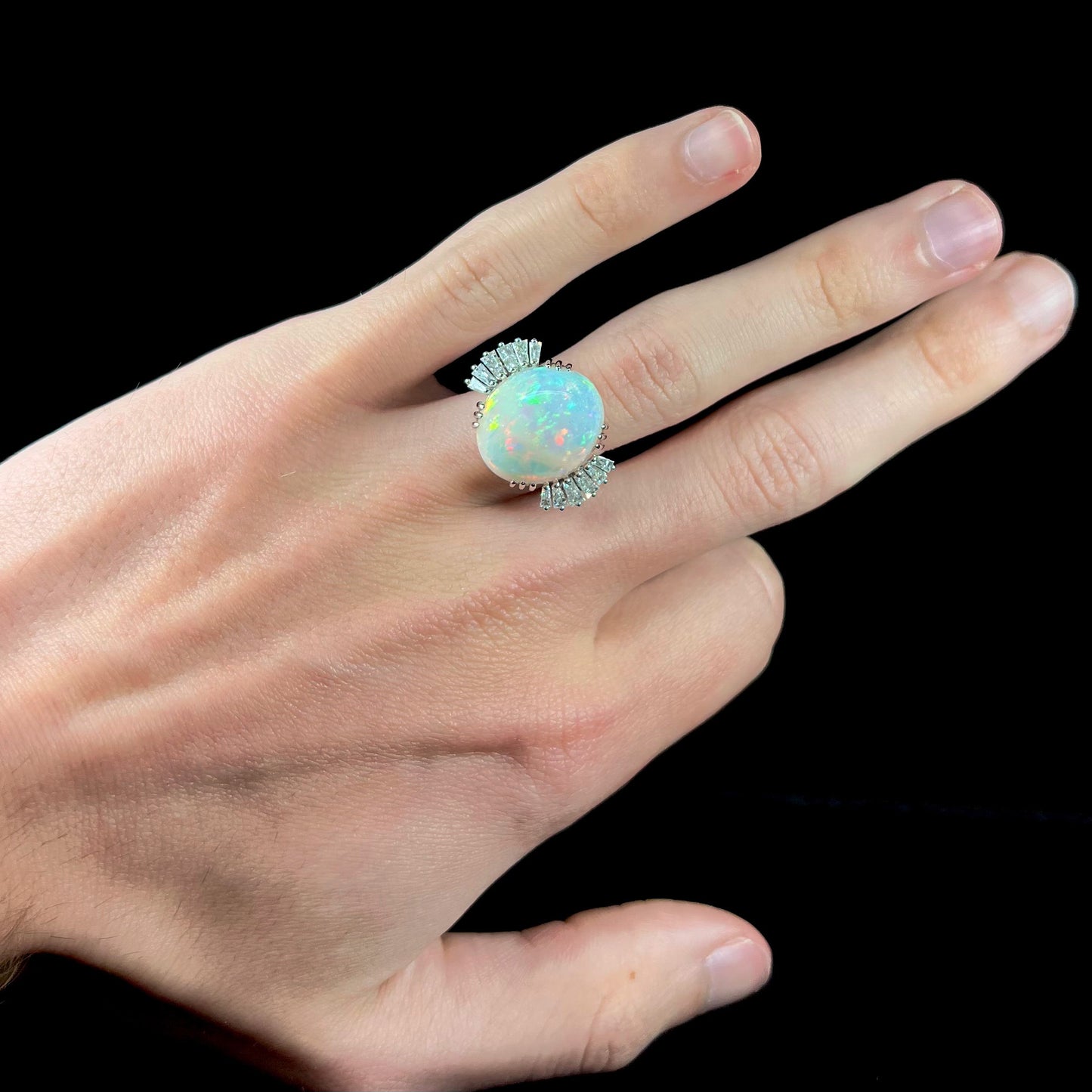 An oval cabochon cut opal mounted in a ladies' white gold ring between tapered baguette cut diamonds.