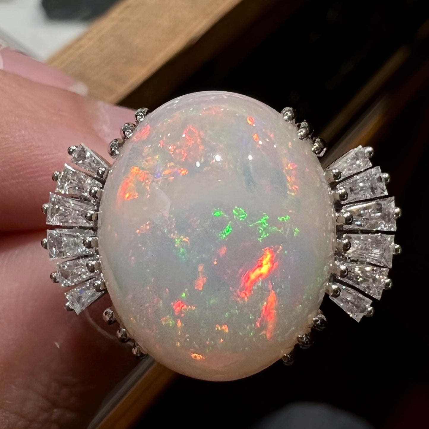 An oval cabochon cut opal mounted in a ladies' white gold ring between tapered baguette cut diamonds.