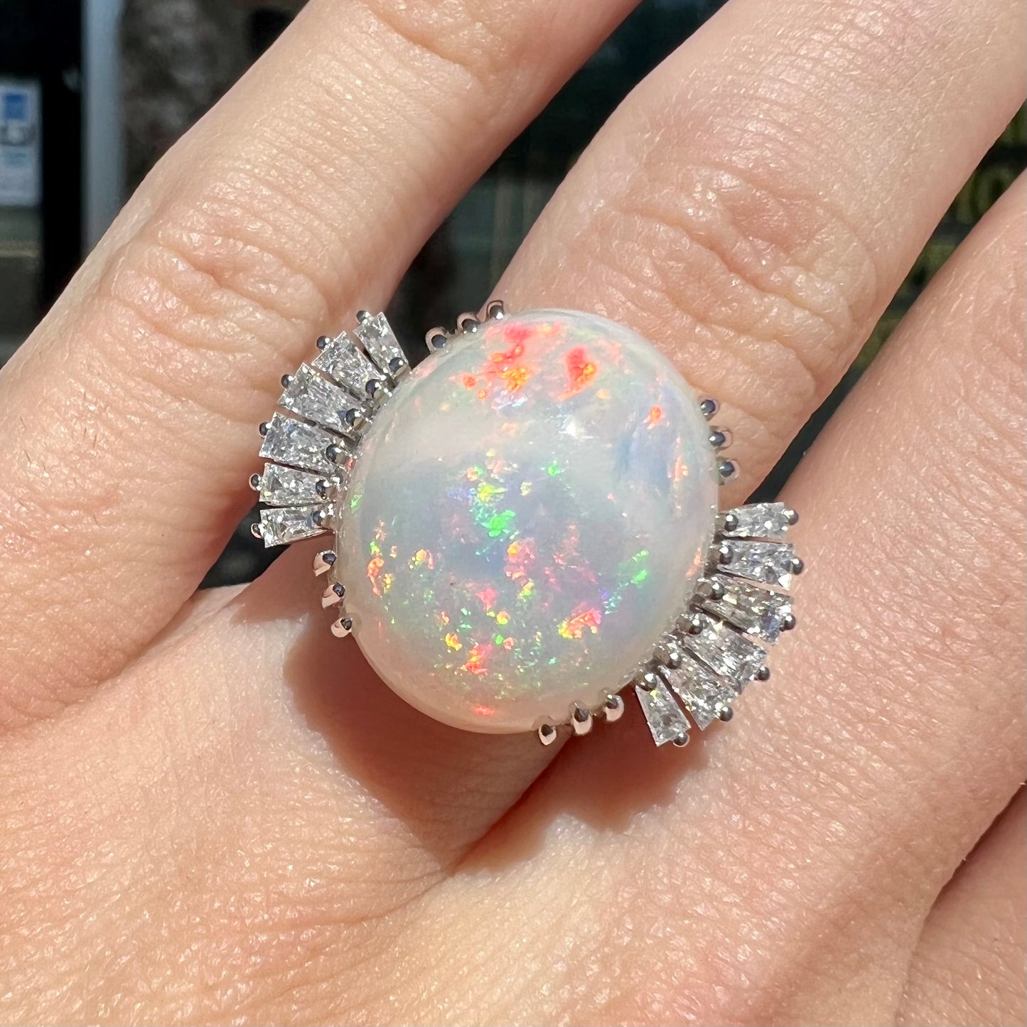 An oval cabochon cut opal mounted in a ladies' white gold ring between tapered baguette cut diamonds.