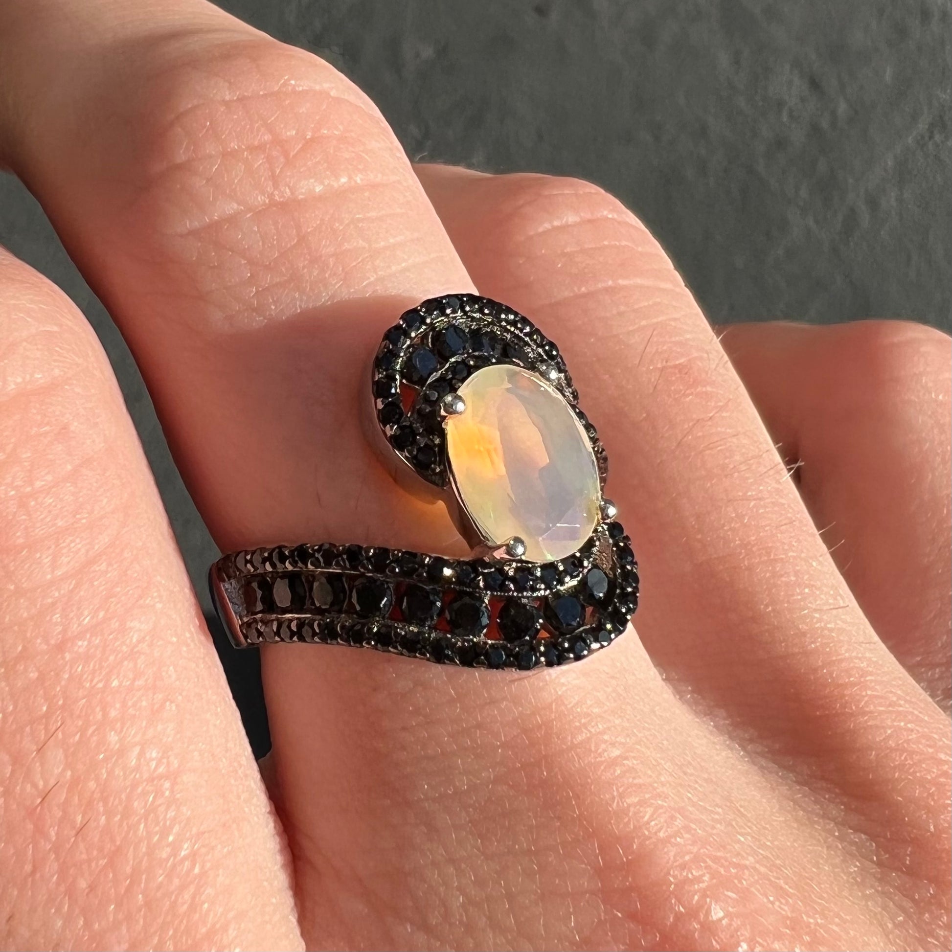 A sterling silver ring set with round black spinel stones and an oval cut, faceted Ethiopian opal.