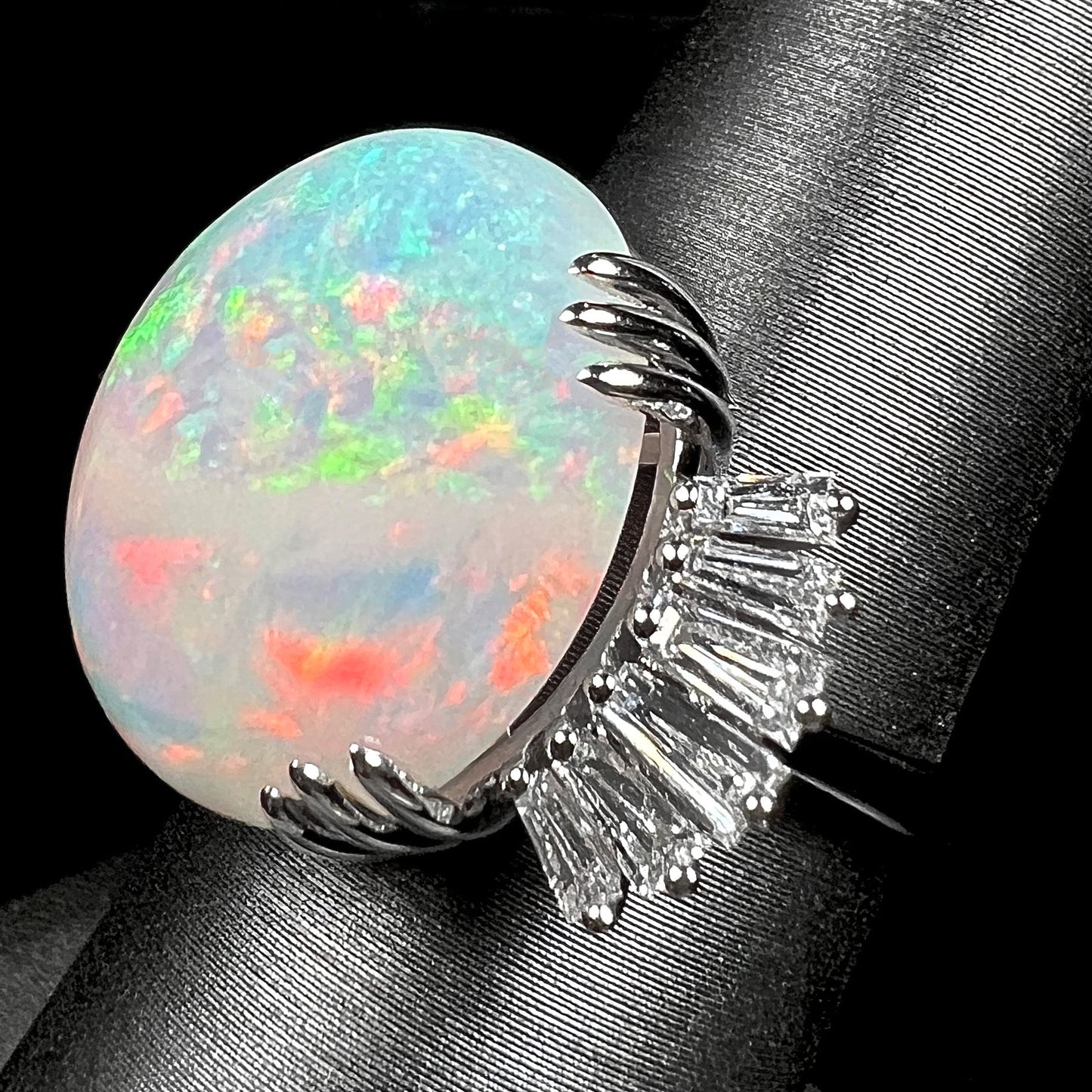 An oval cabochon cut opal mounted in a ladies' white gold ring between tapered baguette cut diamonds.