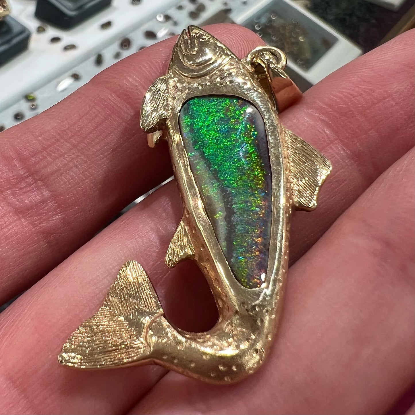 A yellow gold fish pendant detailed to look like a rainbow trout.  The body of the fish is set with a color changing black opal stone.