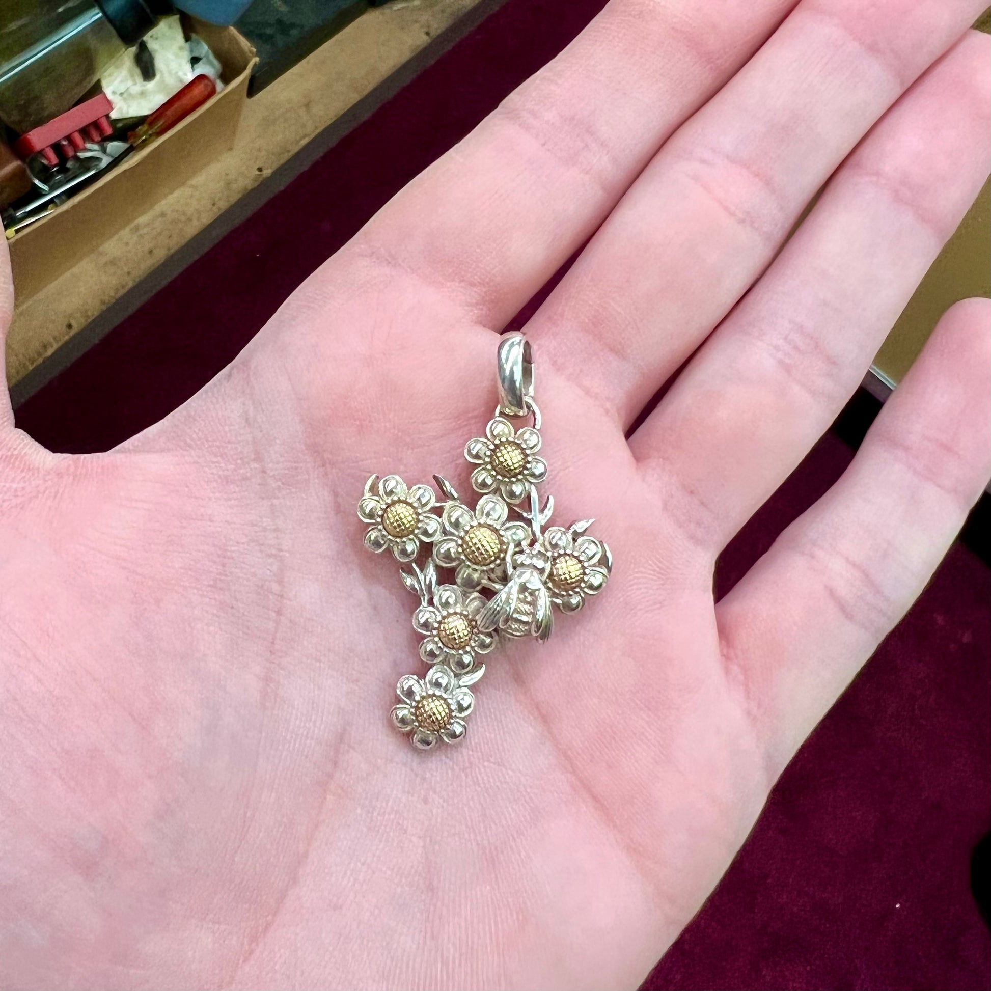 A cross pendant with floral decoration.  The cross is made of six  flowers with sterling silver petals and yellow gold nectar.  A silver bee is on one of the pendants.  The bail opens and closes.
