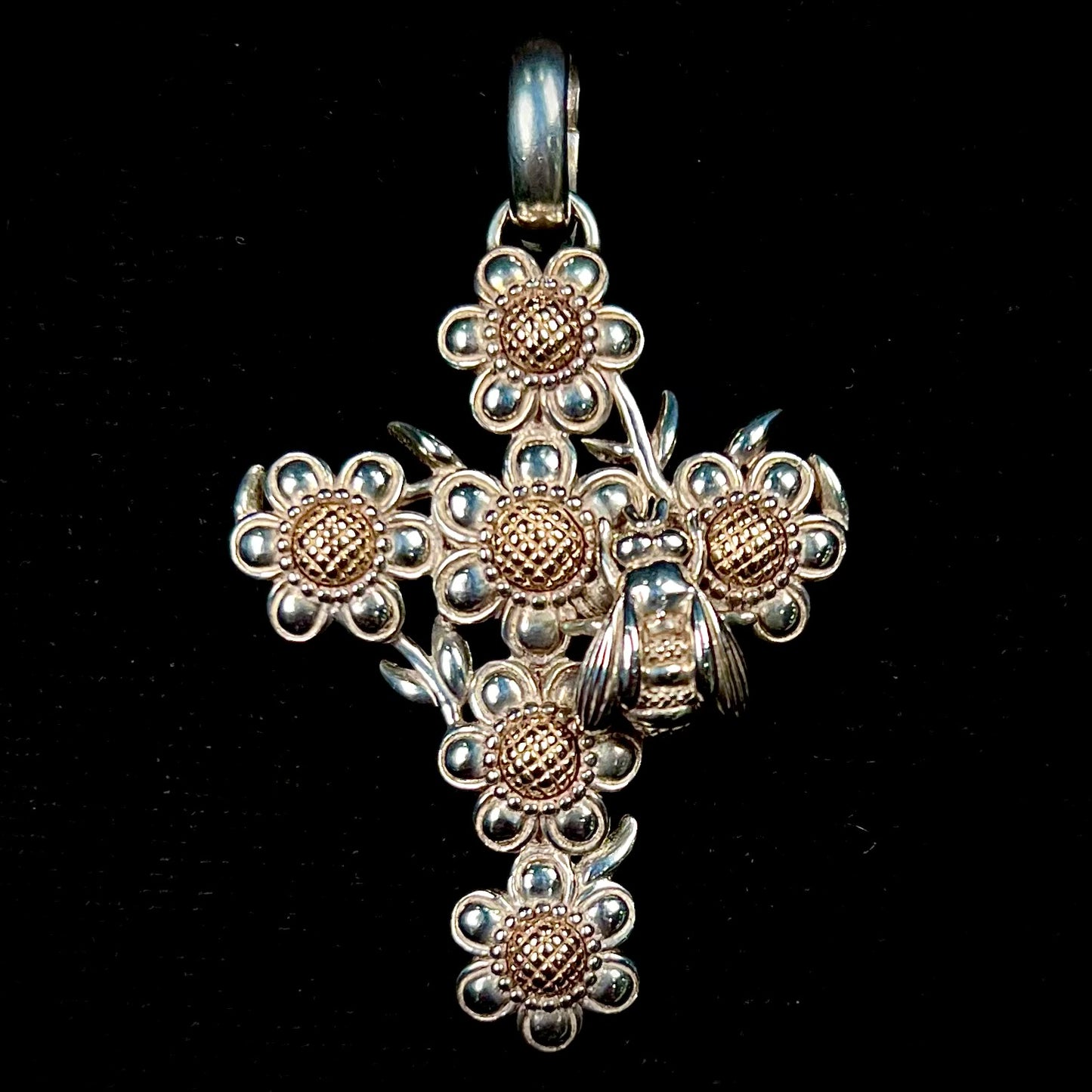 A cross pendant with floral decoration.  The cross is made of six  flowers with sterling silver petals and yellow gold nectar.  A silver bee is on one of the pendants.  The bail opens and closes.