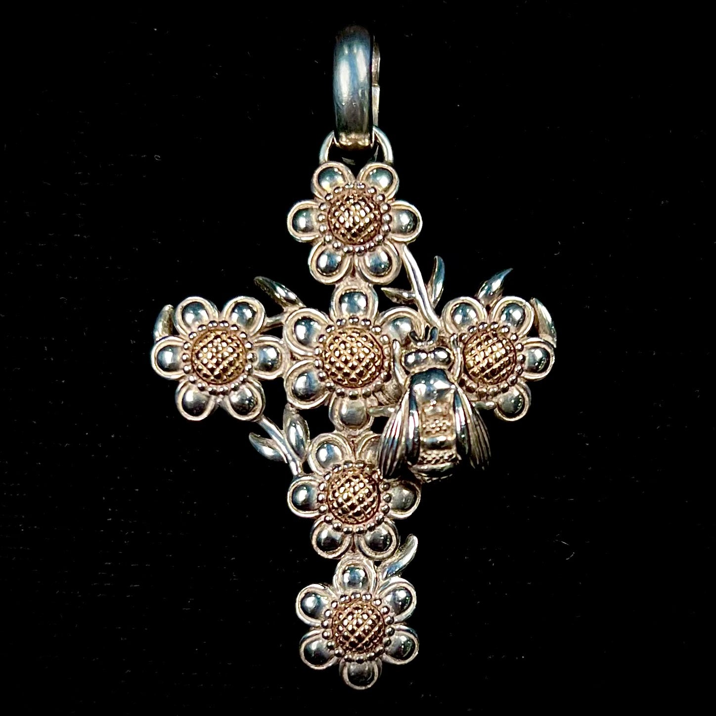 A cross pendant with floral decoration.  The cross is made of six  flowers with sterling silver petals and yellow gold nectar.  A silver bee is on one of the pendants.  The bail opens and closes.