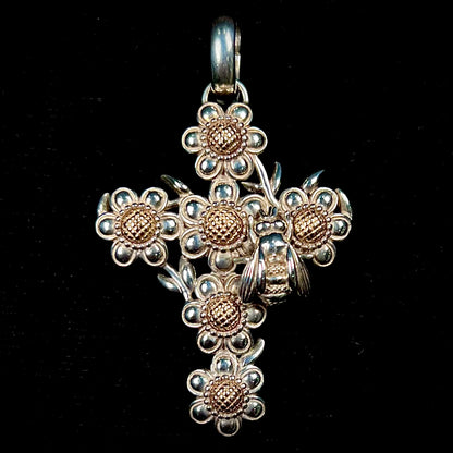 A cross pendant with floral decoration.  The cross is made of six  flowers with sterling silver petals and yellow gold nectar.  A silver bee is on one of the pendants.  The bail opens and closes.