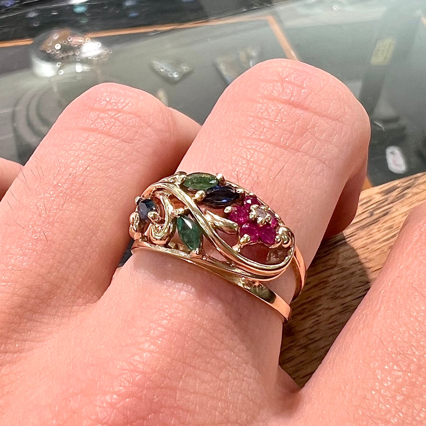 A yellow gold ladies' ring featuring the motif of a flower with leaves set with emeralds, rubies, sapphires, and a  diamond.