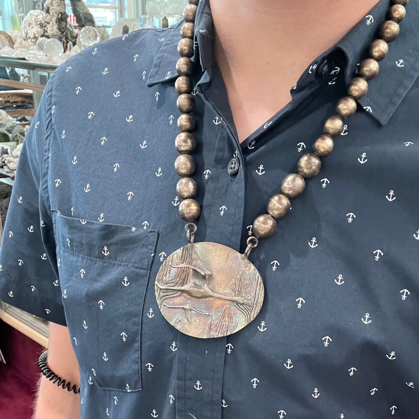 A handmade sterling silver bead necklace with a rainbow patinaed medallion that features 3D cast flamingos flying through a cactus desert.