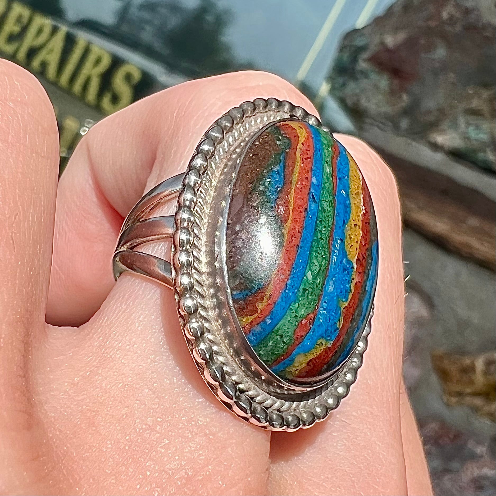 A split shank, rope bezel set silver ring set with an oval cut fordite paint stone.