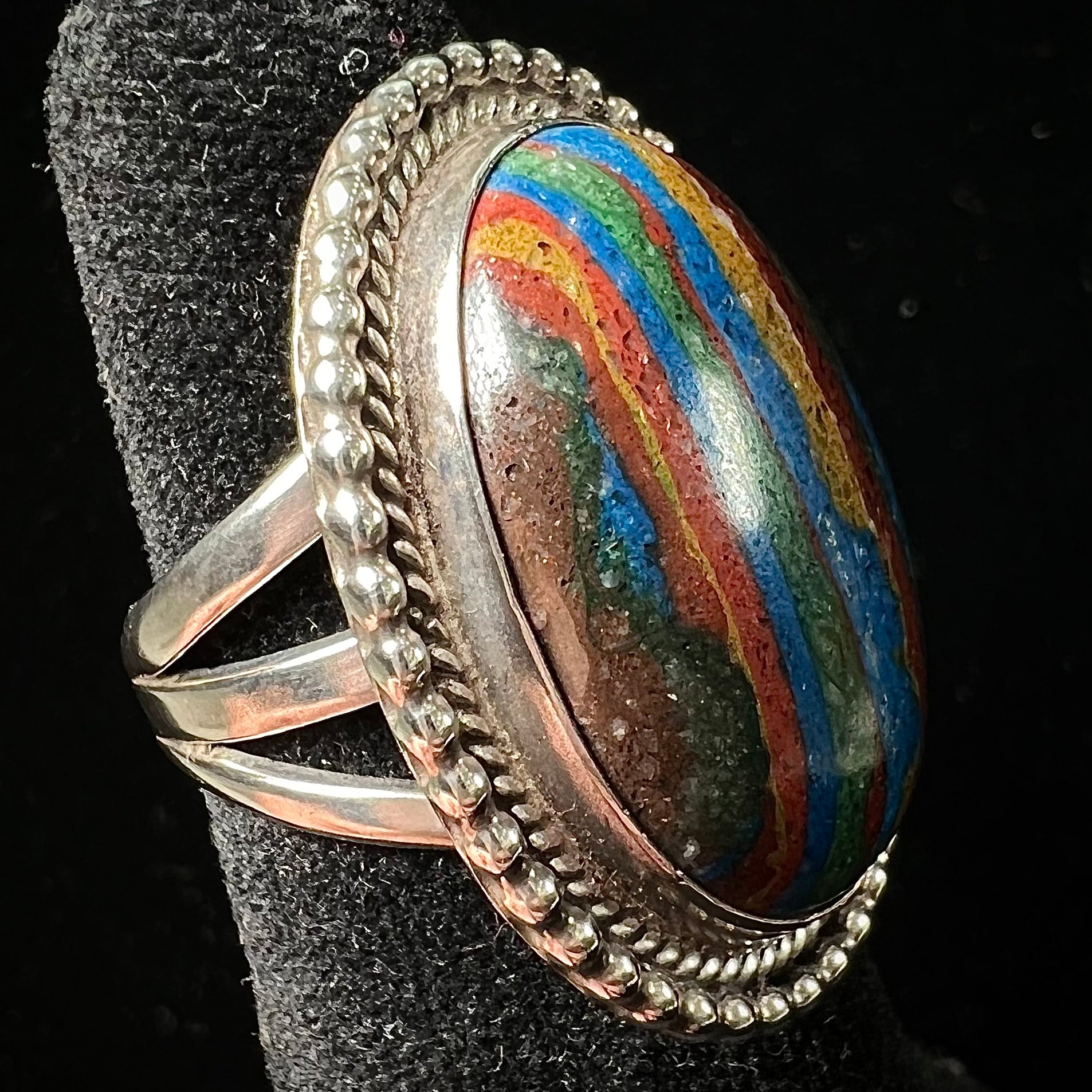 A split shank, rope bezel set silver ring set with an oval cut fordite paint stone.