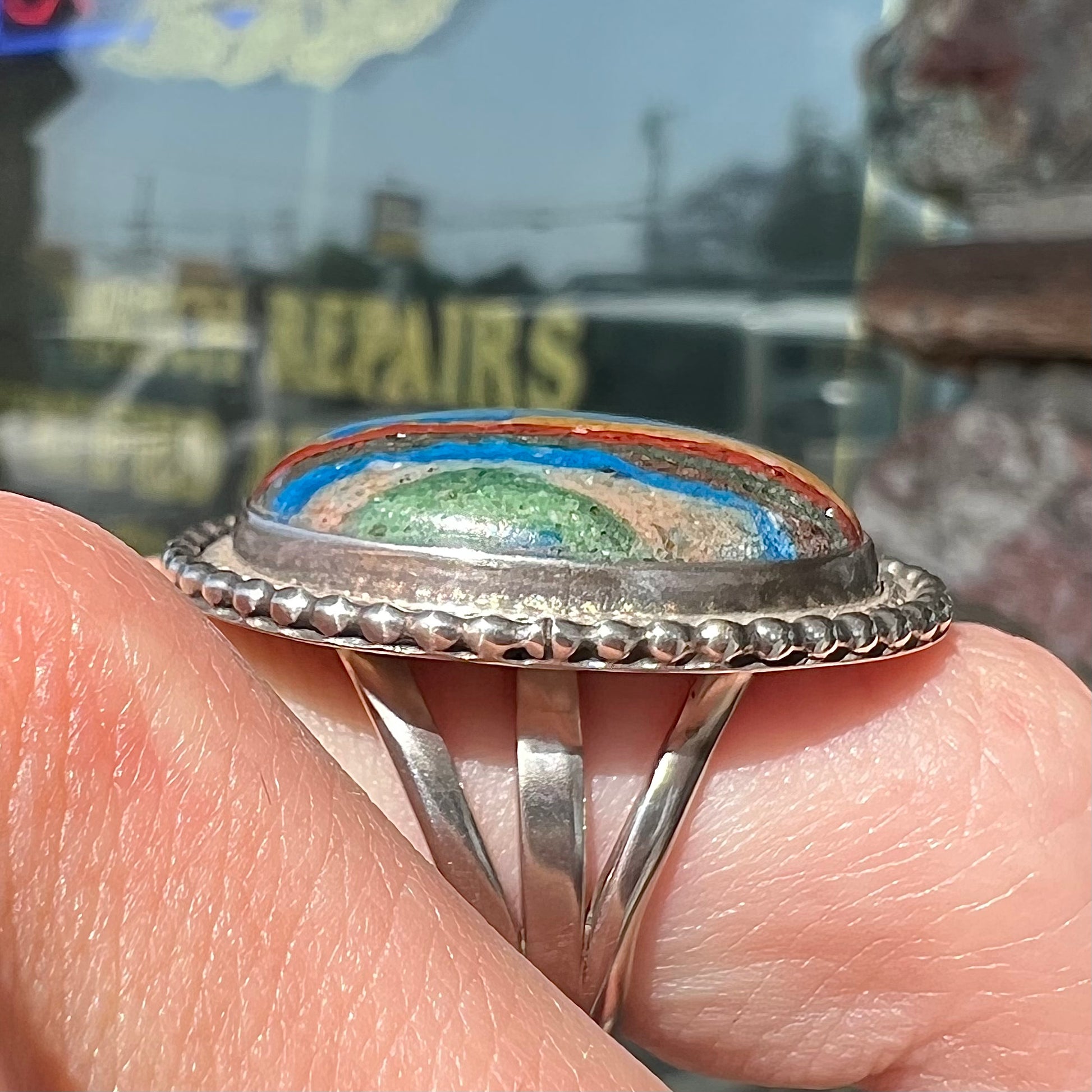 A split shank, rope bezel set silver ring set with an oval cut fordite paint stone.