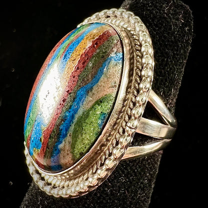 A split shank, rope bezel set silver ring set with an oval cut fordite paint stone.