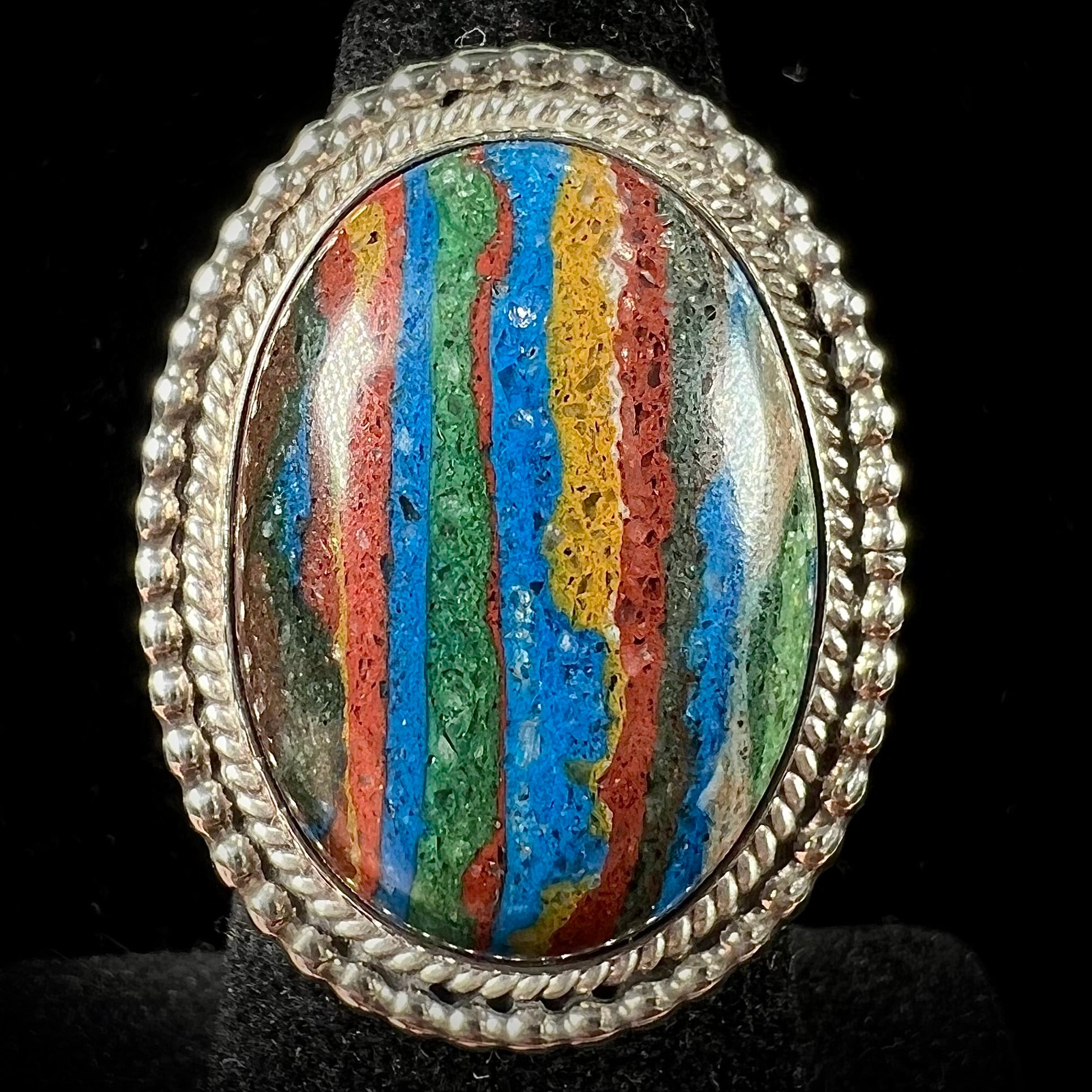 A split shank, rope bezel set silver ring set with an oval cut fordite paint stone.