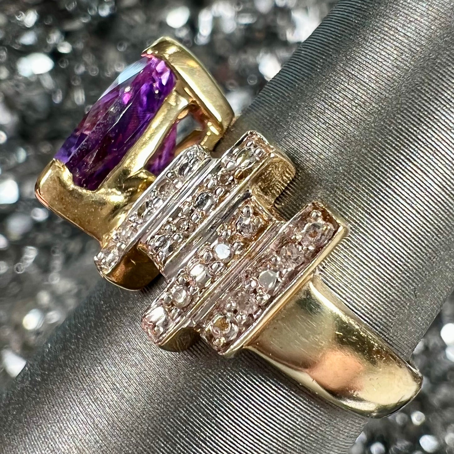 A yellow gold ring set with a trillion cut amethyst and round diamond accent stones.