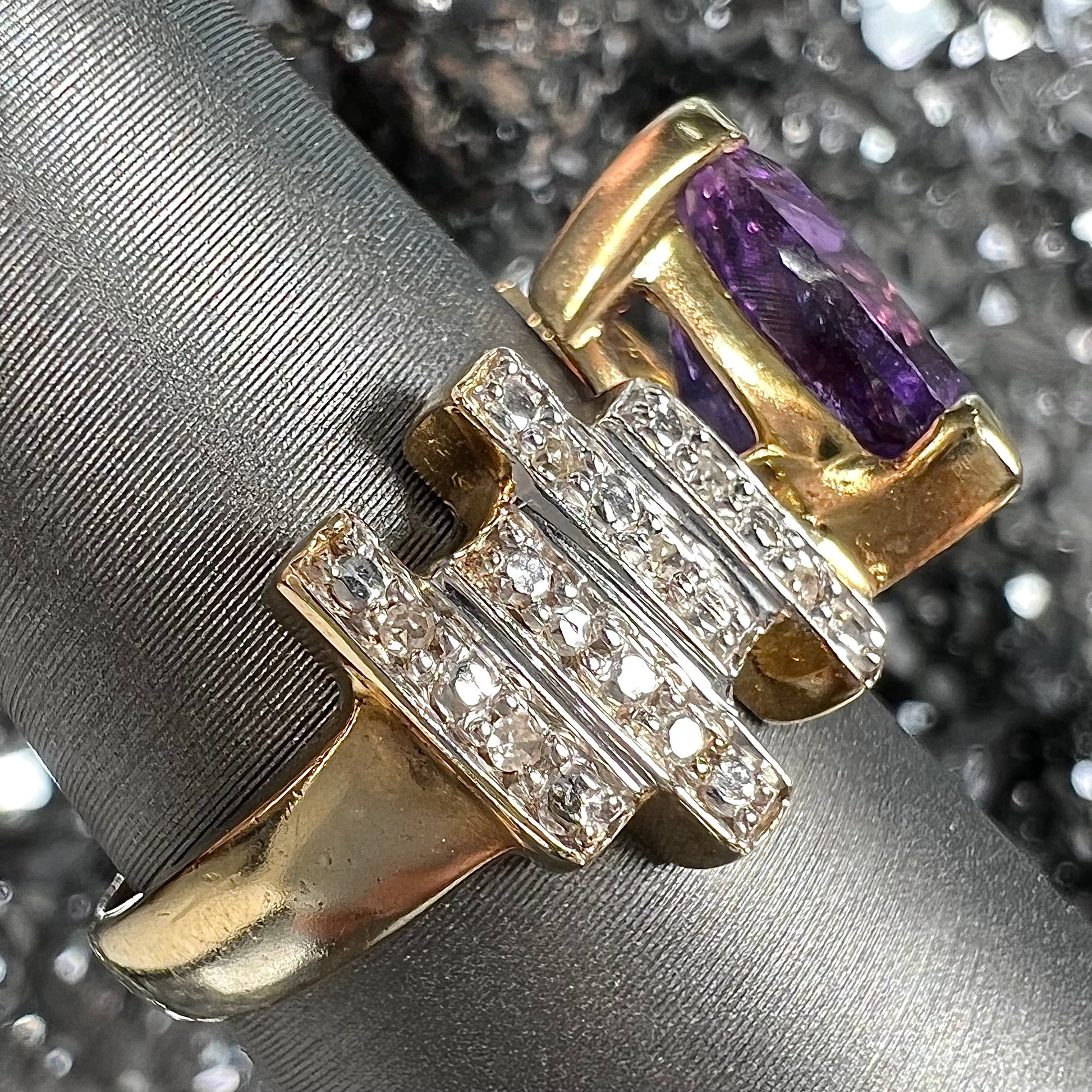 A yellow gold ring set with a trillion cut amethyst and round diamond accent stones.