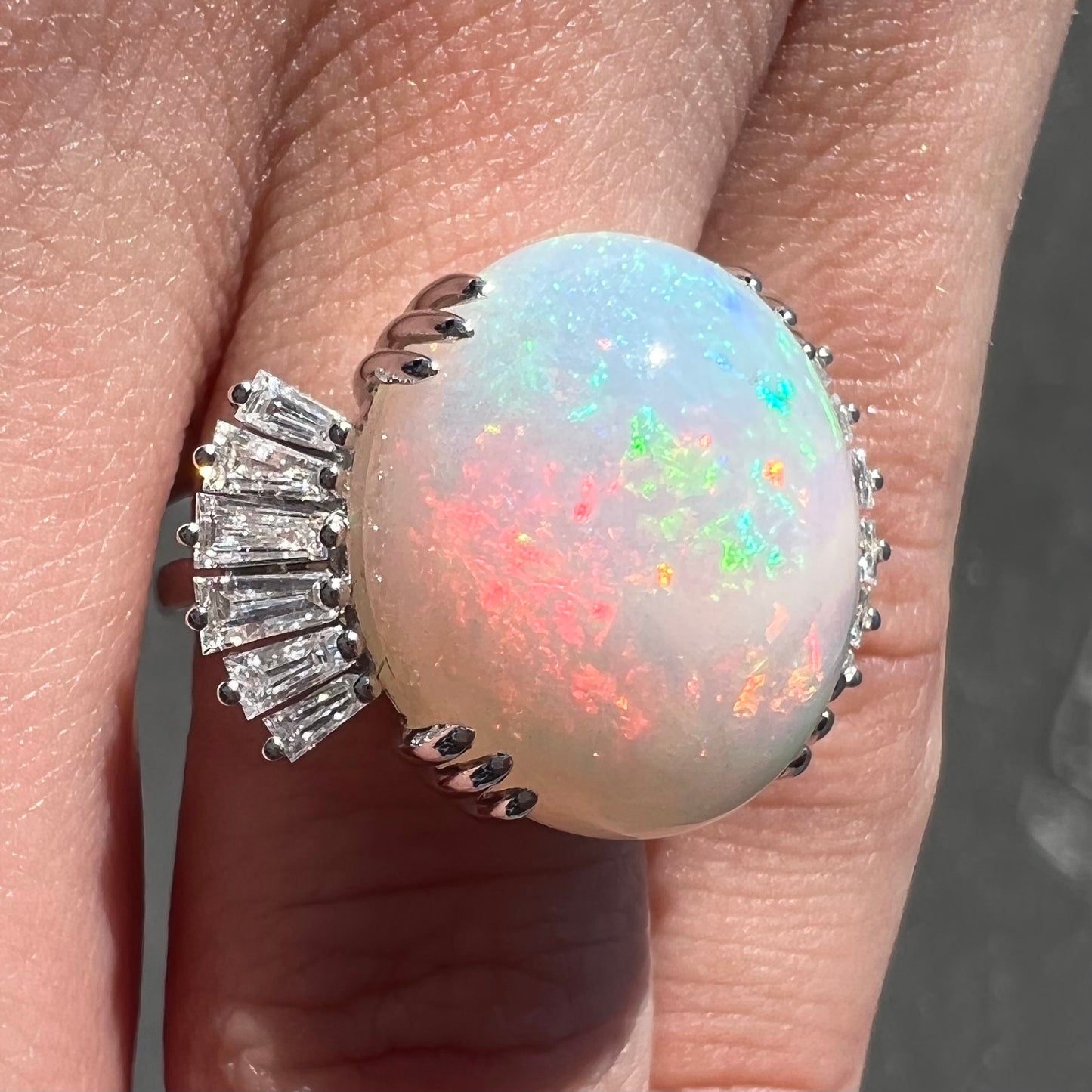 An oval cabochon cut opal mounted in a ladies' white gold ring between tapered baguette cut diamonds.