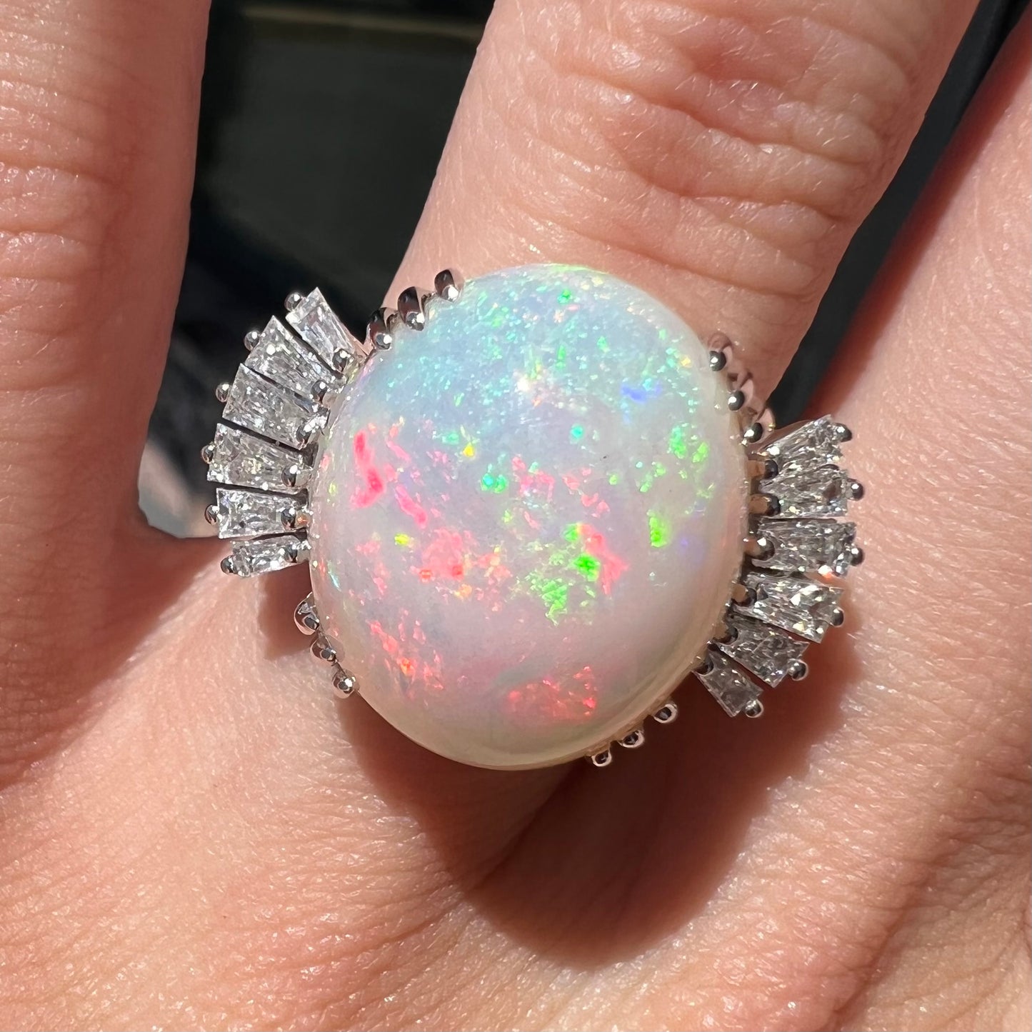 An oval cabochon cut opal mounted in a ladies' white gold ring between tapered baguette cut diamonds.