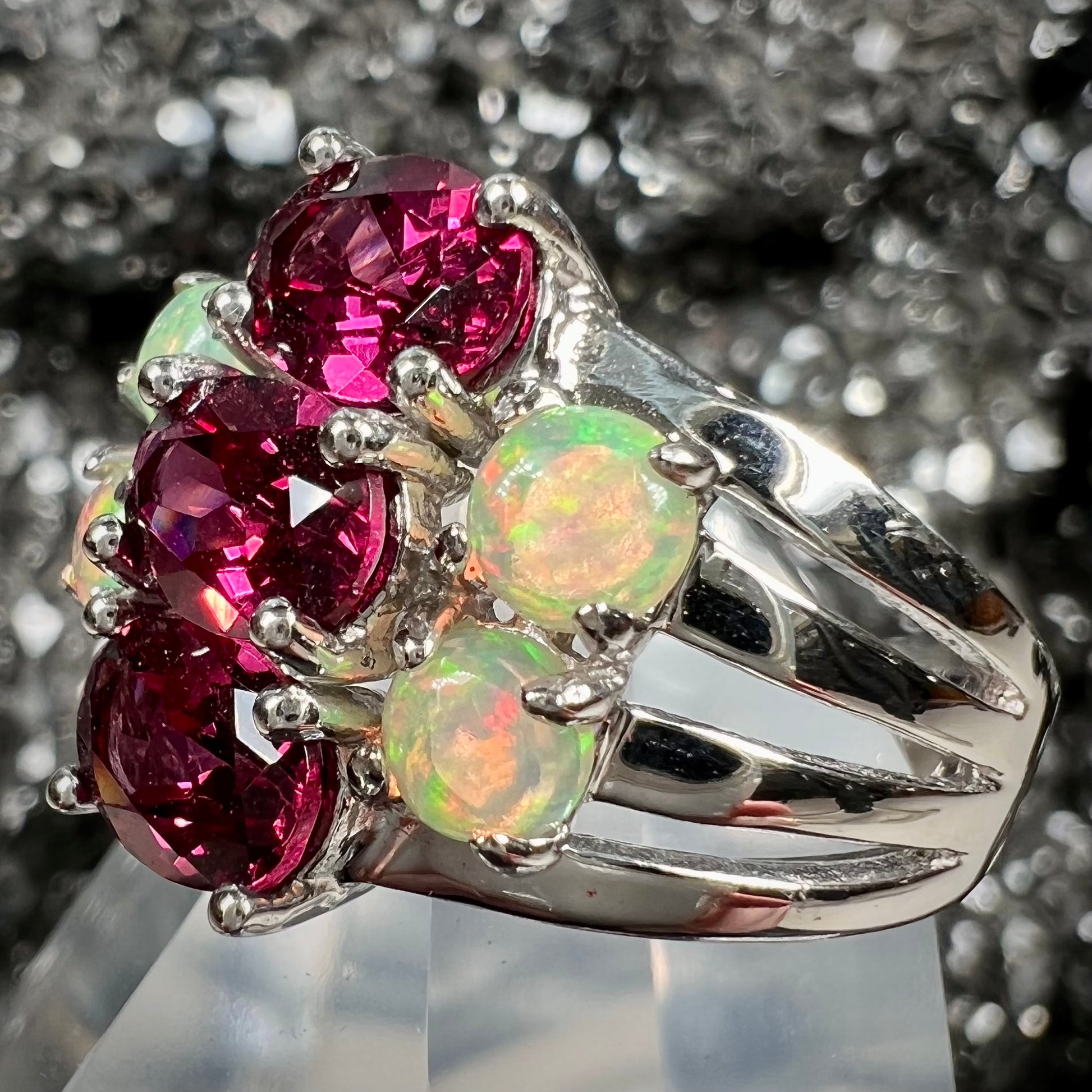 A sterling silver ring set with three oval cut rhodolite garnets and four round cabochon cut Ethiopian opals.