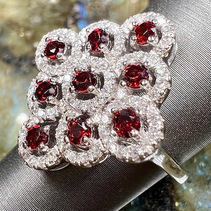 A sterling silver cluster ring set with round almandine garnet main stones and white zircon accents.