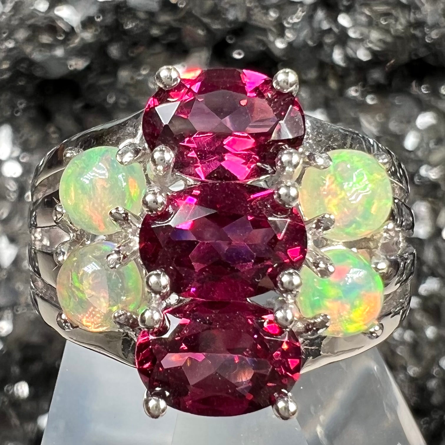 A sterling silver ring set with three oval cut rhodolite garnets and four round cabochon cut Ethiopian opals.