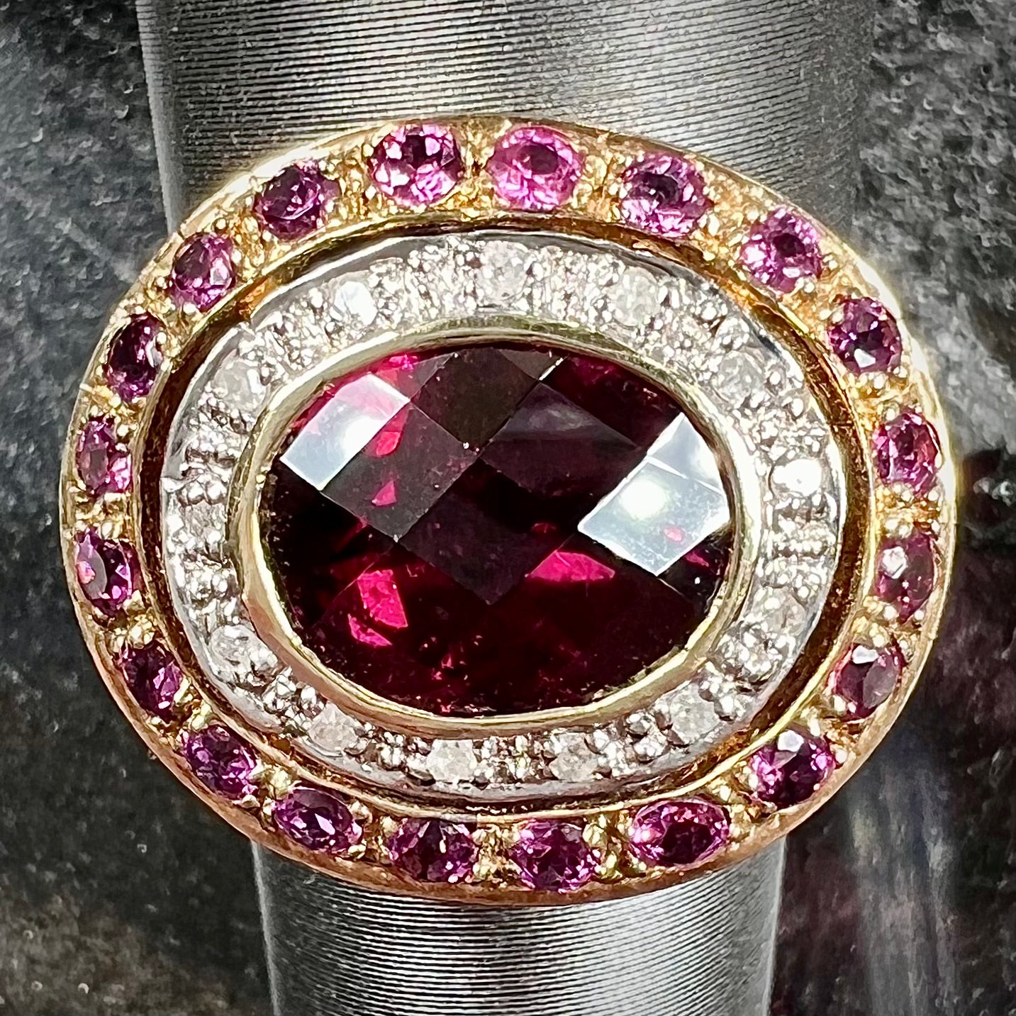 A yellow gold garnet and diamond halo ring set with a checkerboard cut rhodolite garnet center stone.
