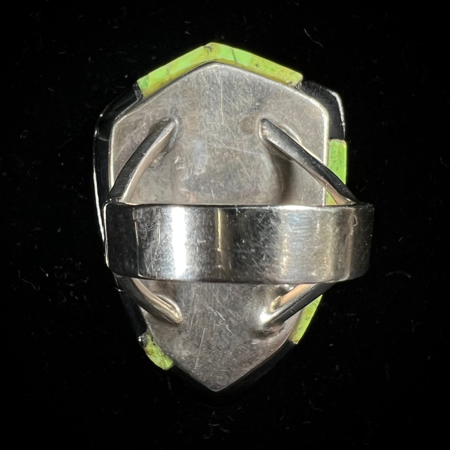 A shield shaped silver ring bezel set with a green gaspeite stone with stone inlaid edges, handmade by artist Benny Armijo.