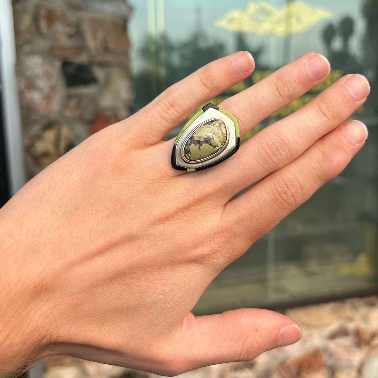 A shield shaped silver ring bezel set with a green gaspeite stone with stone inlaid edges, handmade by artist Benny Armijo.