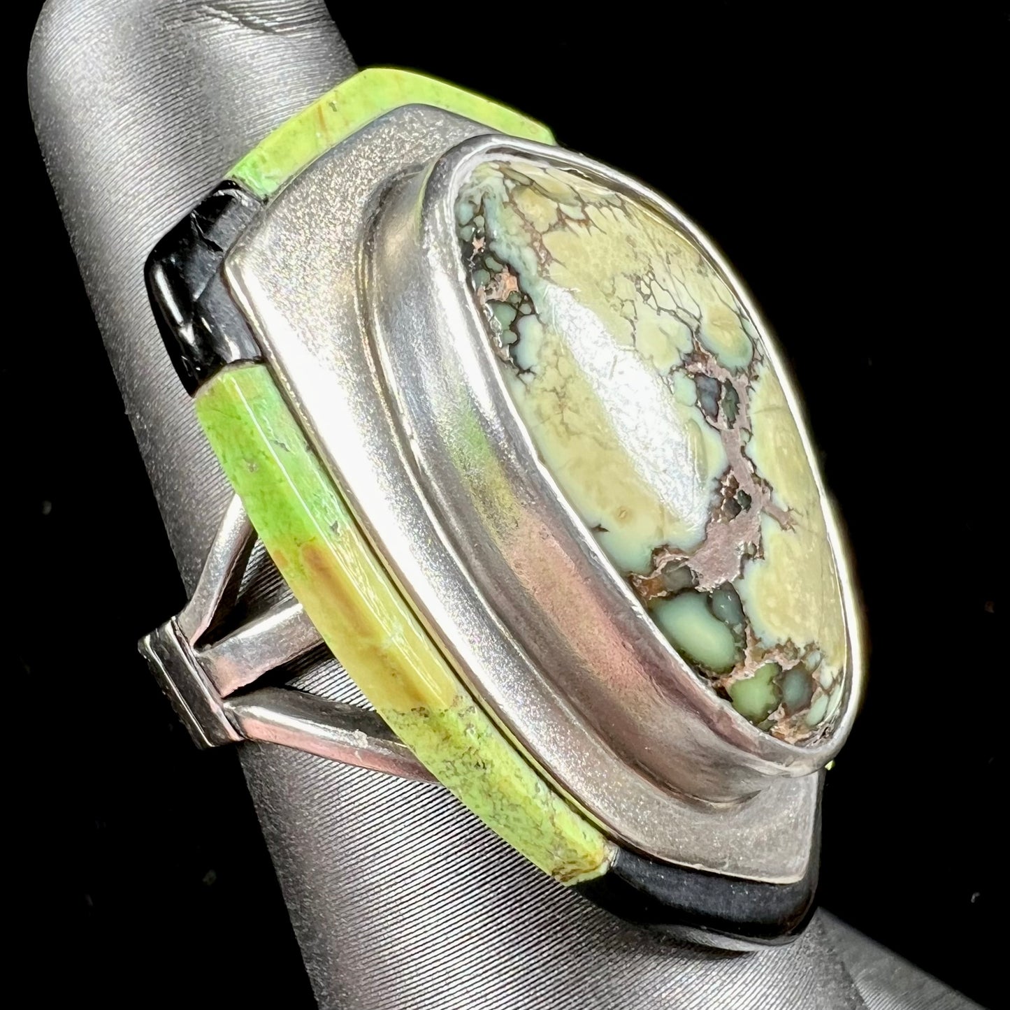 A shield shaped silver ring bezel set with a green gaspeite stone with stone inlaid edges, handmade by artist Benny Armijo.