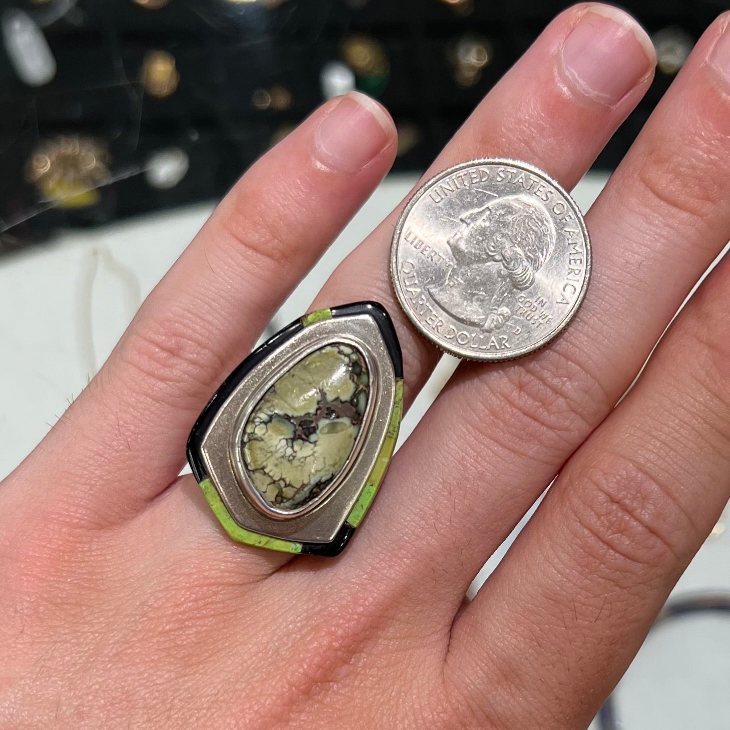A shield shaped silver ring bezel set with a green gaspeite stone with stone inlaid edges, handmade by artist Benny Armijo.