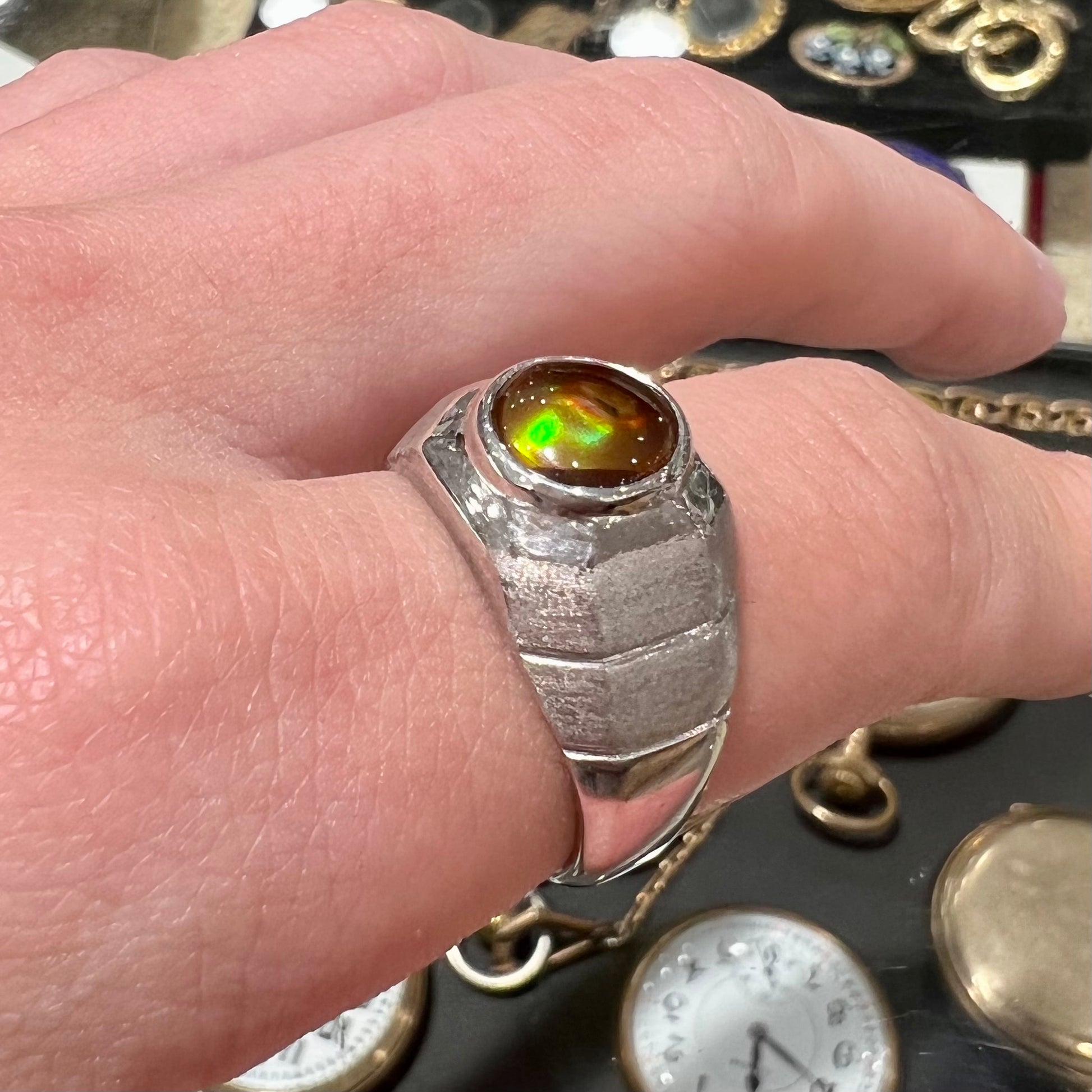 A round cabochon cut red and green fire agate set in a brushed metal white gold men's ring.