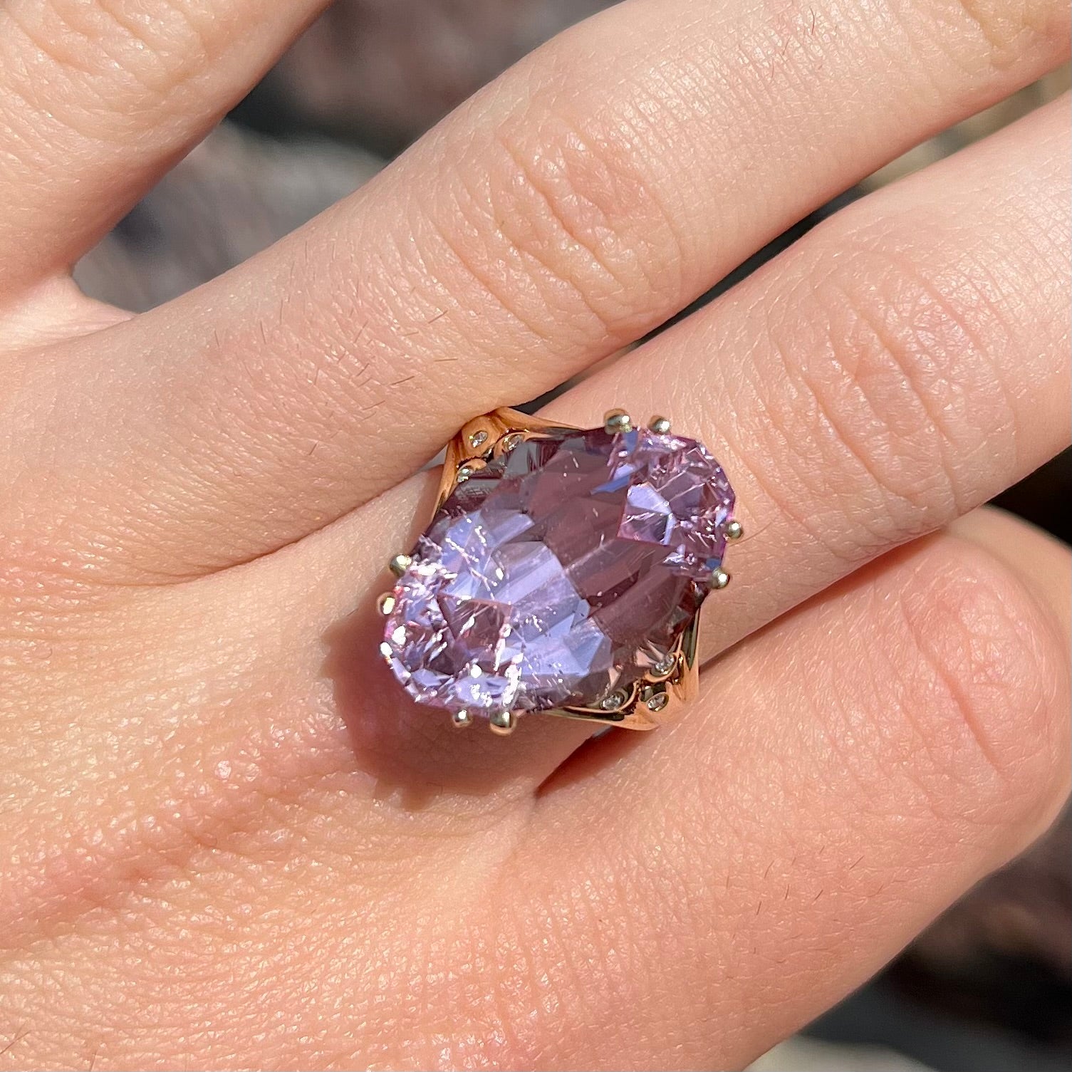 A large, pink kunzite is prong set into a 14kt yellow gold basket-style ring mounting with three diamonds flush set into the design on each side.