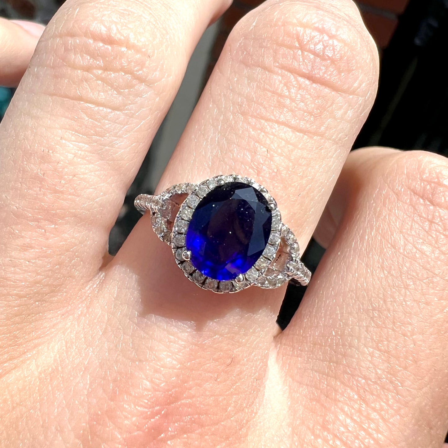 A sterling silver, white zircon halo ring set with an oval cut blue sapphire.