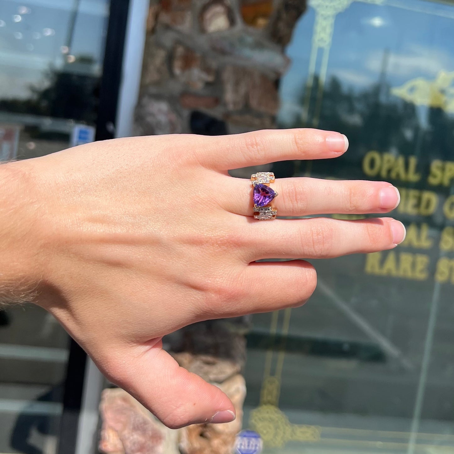 A yellow gold ring set with a trillion cut amethyst and round diamond accent stones.