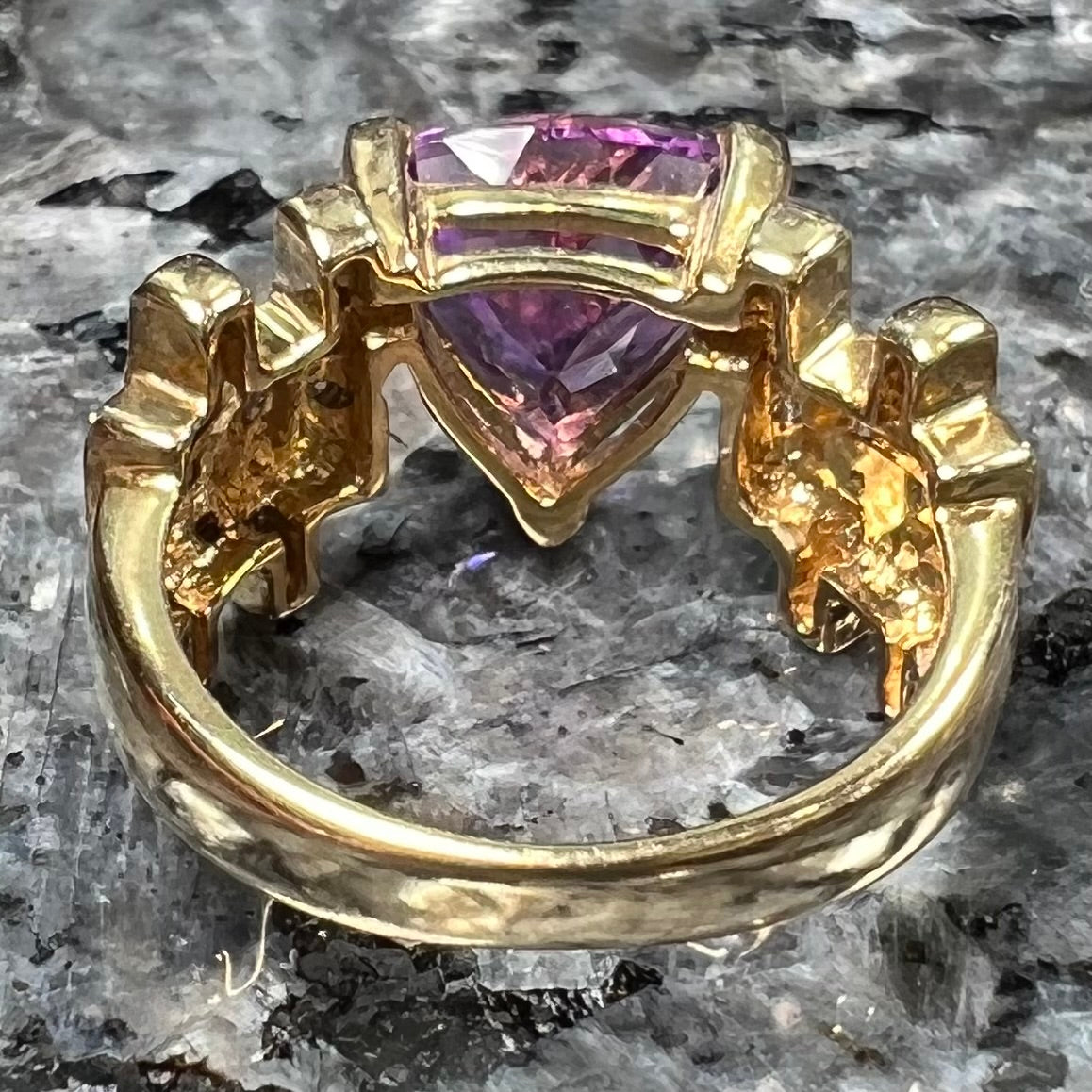 A yellow gold ring set with a trillion cut amethyst and round diamond accent stones.