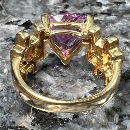 A yellow gold ring set with a trillion cut amethyst and round diamond accent stones.