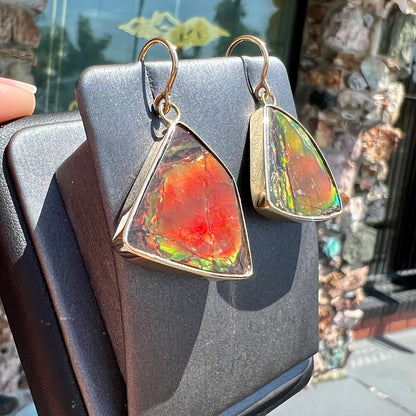 Yellow gold French wire dangle earrings bezel set with two polished freeform cut red ammolite fossils.