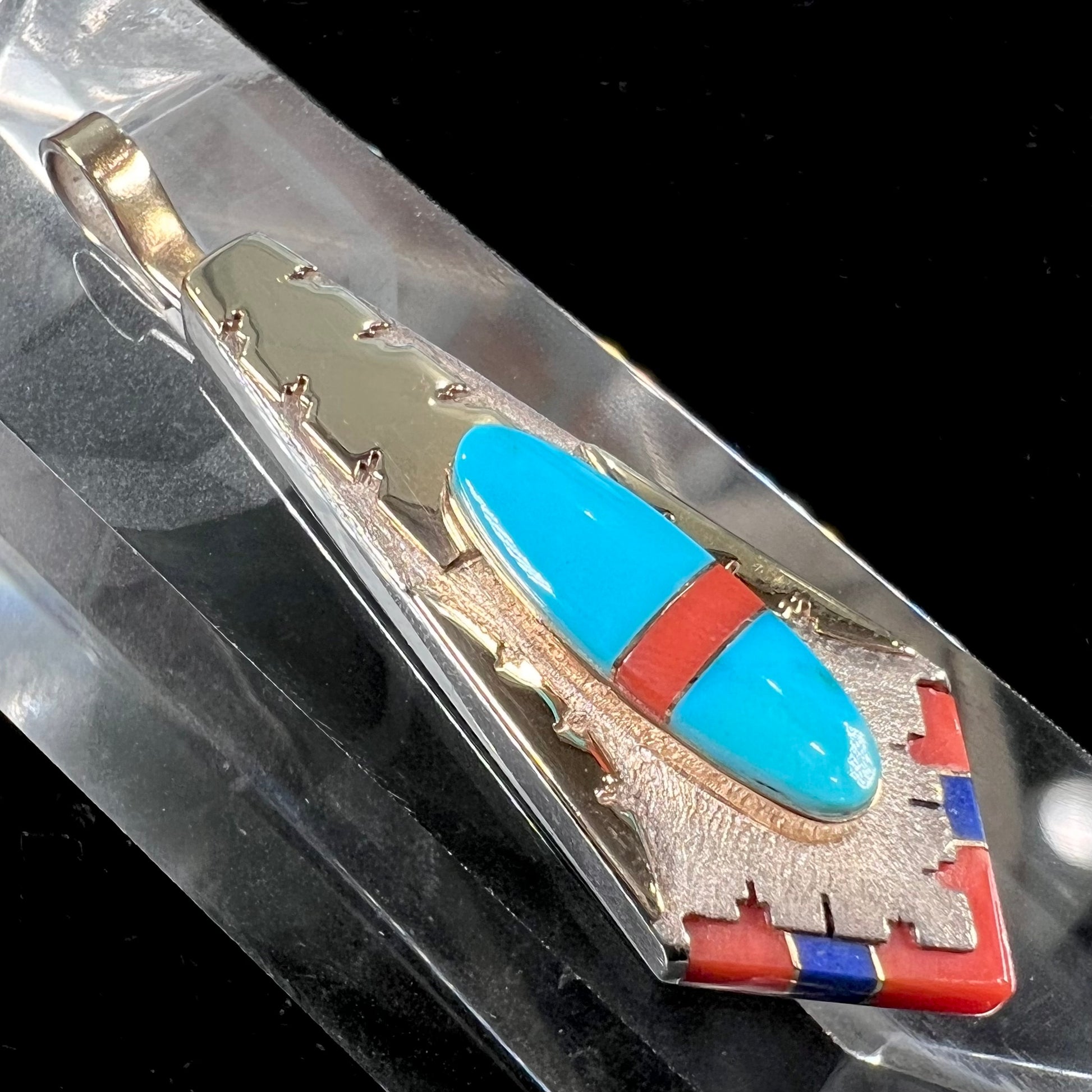 A yellow gold and sterling silver pendant inlaid with turquoise, coral, and lapis lazuli stones.  The piece is made by an unknown Native American artist and signed with the initials "LY".