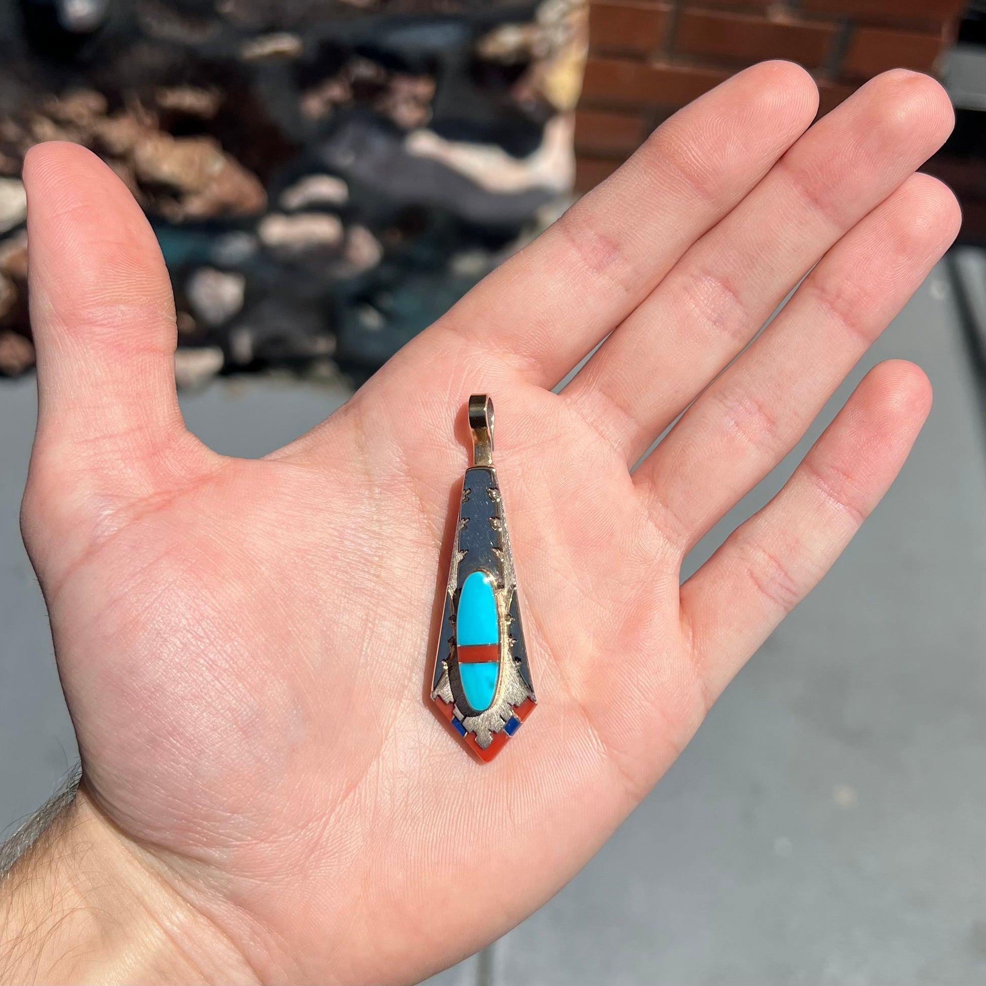 A yellow gold and sterling silver pendant inlaid with turquoise, coral, and lapis lazuli stones.  The piece is made by an unknown Native American artist and signed with the initials "LY".