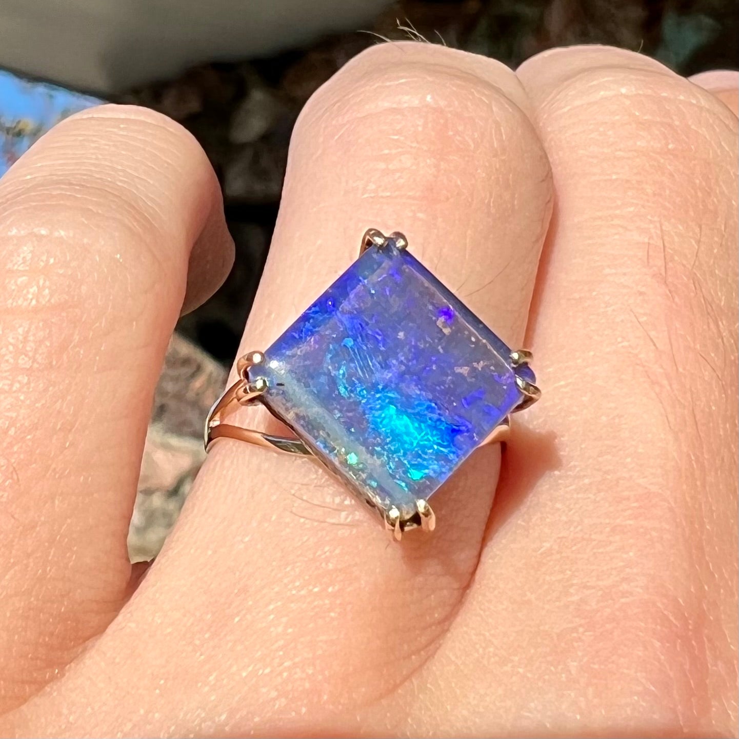 A ladies' boulder opal solitaire ring, handmade in yellow gold.  The stone is purple with flashes of blue, aqua, and green.