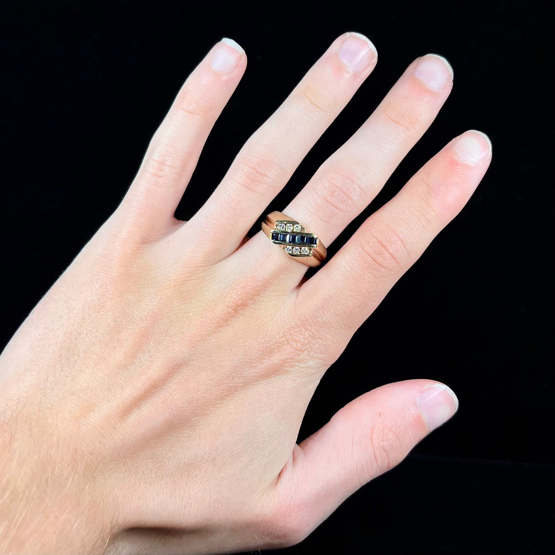 A men's yellow gold ring channel set with princess cut blue sapphires and diamonds.