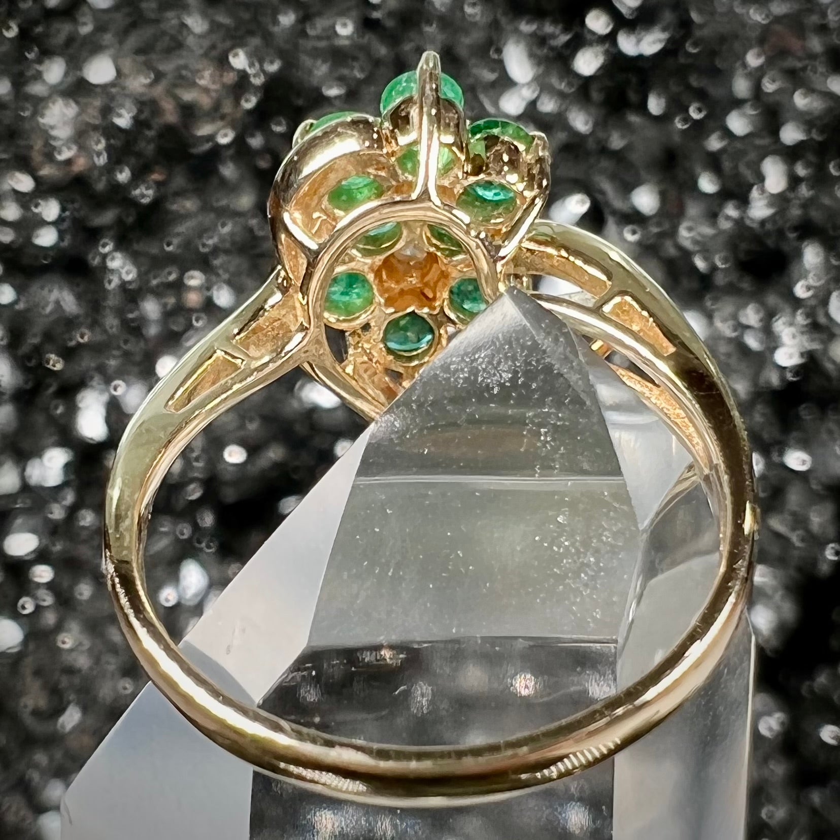 A yellow gold ring set with round cut emerald and diamonds that form the shape of two flowers.