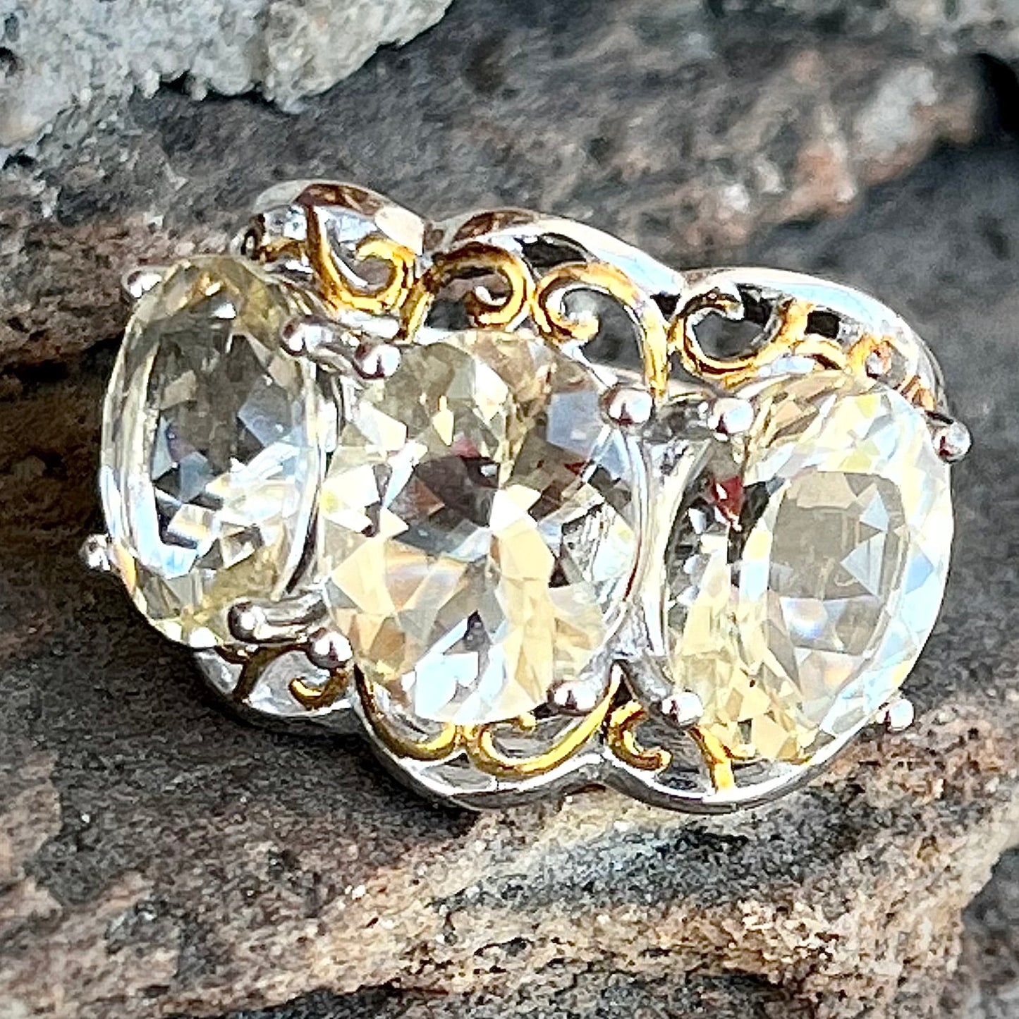 A sterling silver ring set with three oval cut golden beryl stones and yellow gold plated filigree accents.