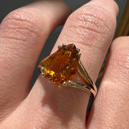 A gold split Euro shank solitaire ring set with an orange pear shape hessonite garnet stone.