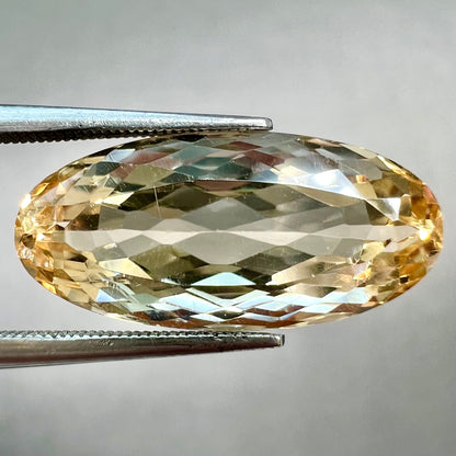 A loose, oval cut golden topaz gemstone.  A stronger concentration of yellow rests in the edges of the stone.
