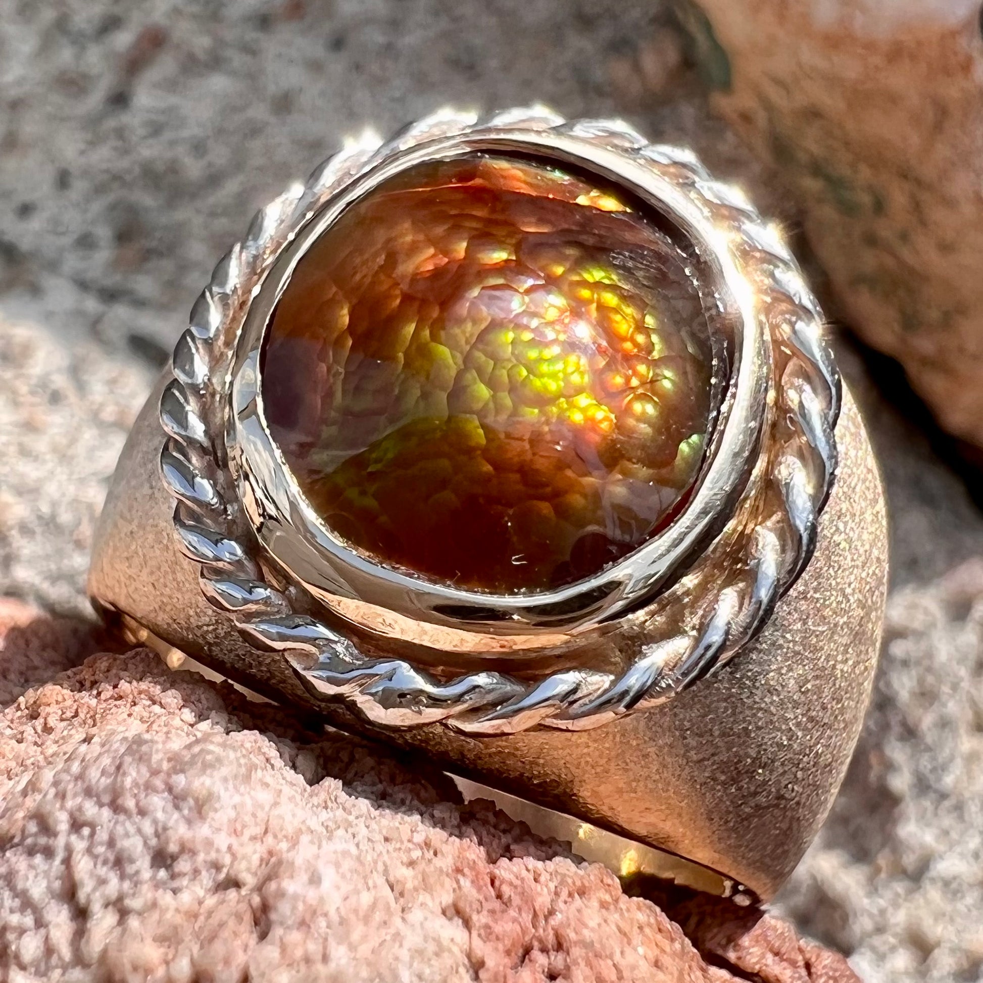 A men's matte finish textured gold fire agate ring.  There is a gold rope bezel around the oval cabochon cut stone.