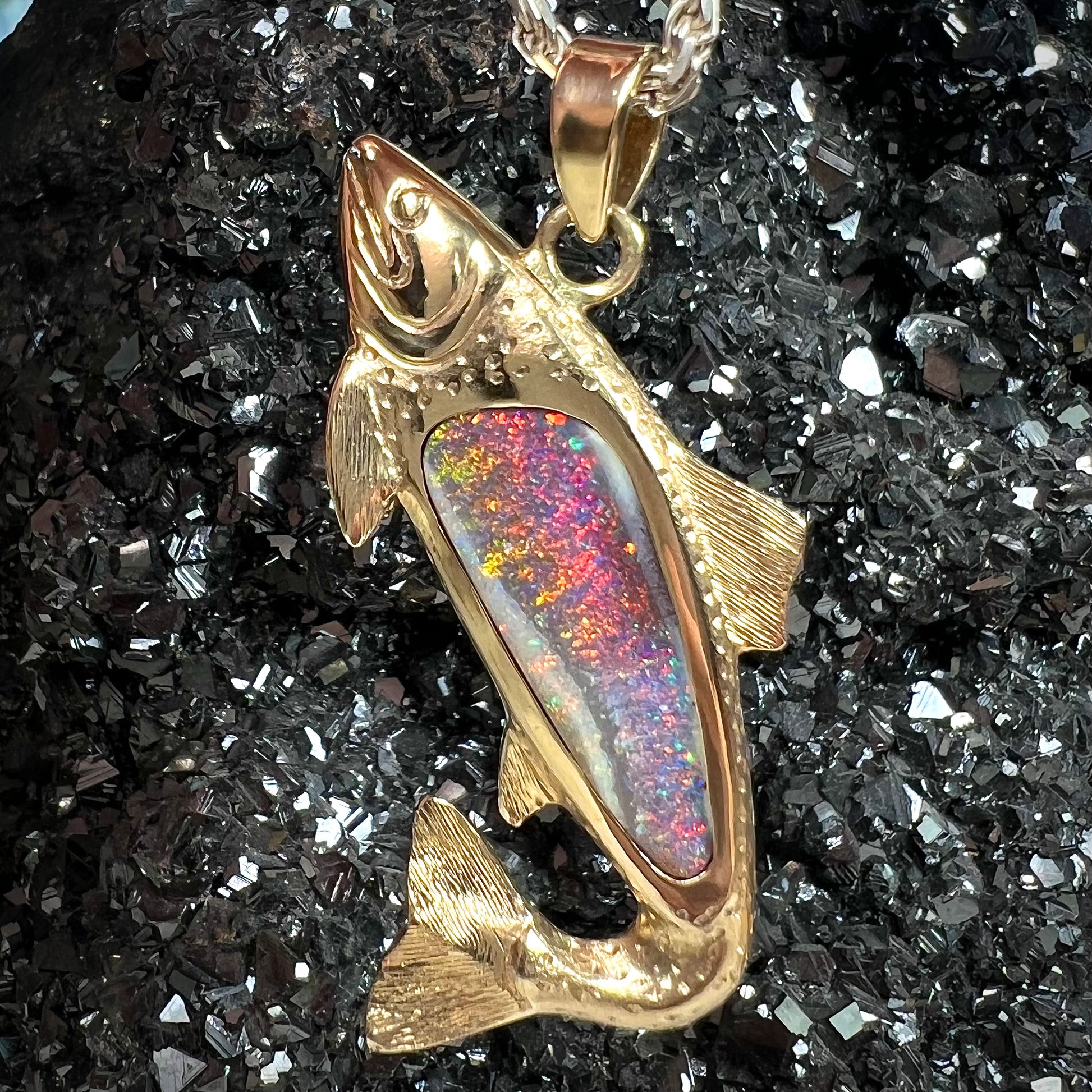 A yellow gold fish pendant detailed to look like a rainbow trout.  The body of the fish is set with a color changing black opal stone.
