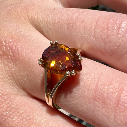 A gold split Euro shank solitaire ring set with an orange pear shape hessonite garnet stone.