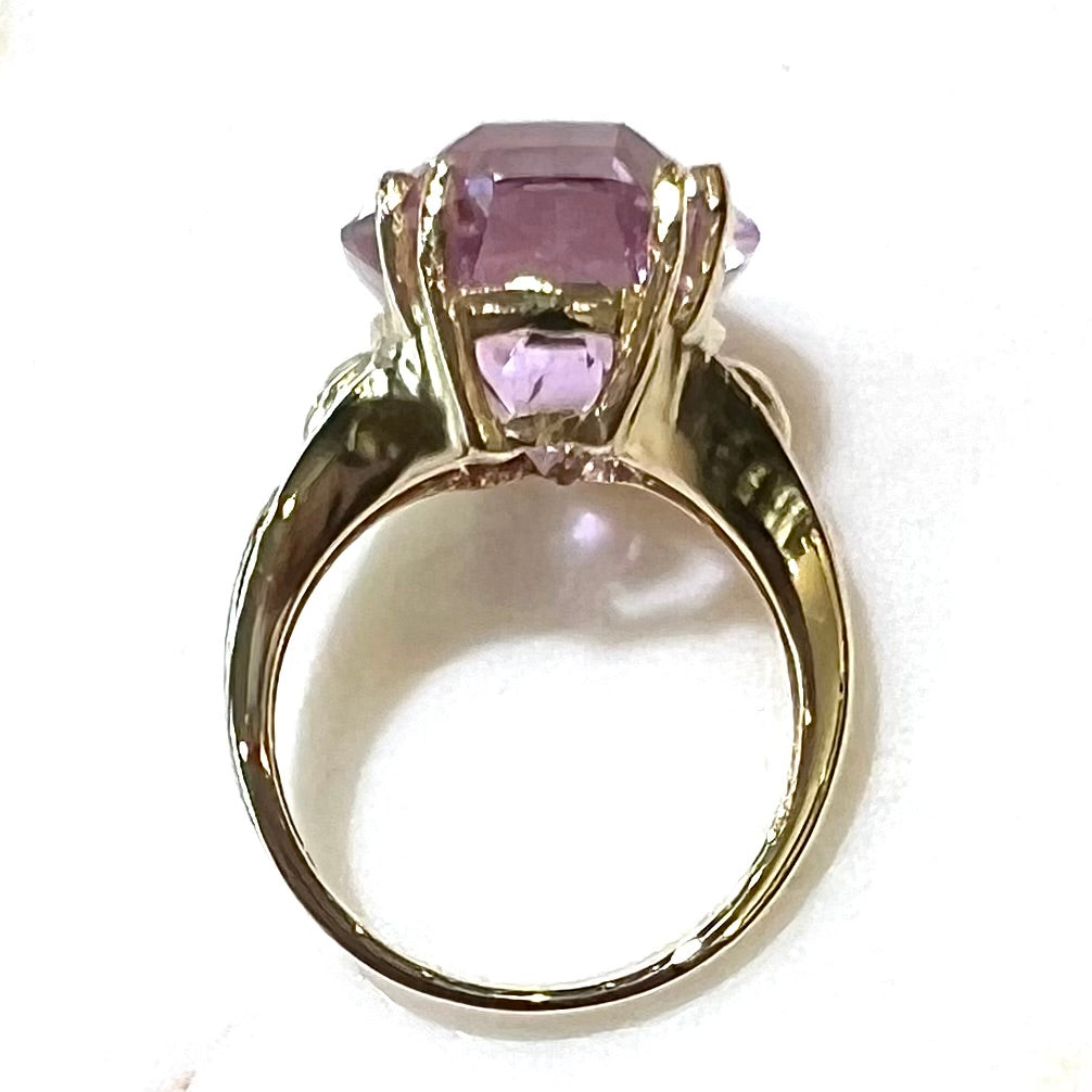 A large, pink kunzite is prong set into a 14kt yellow gold basket-style ring mounting with three diamonds flush set into the design on each side.